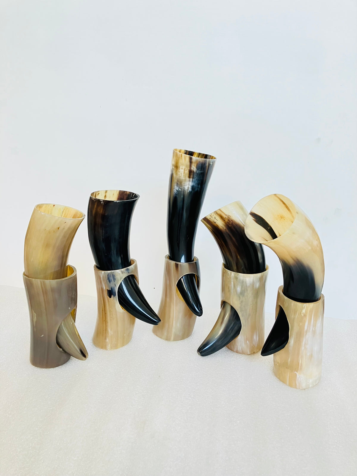 Five handcrafted horn drinking horns with curved shapes, featuring natural tan, cream, and black marbled patterns, displayed on a light neutral background.